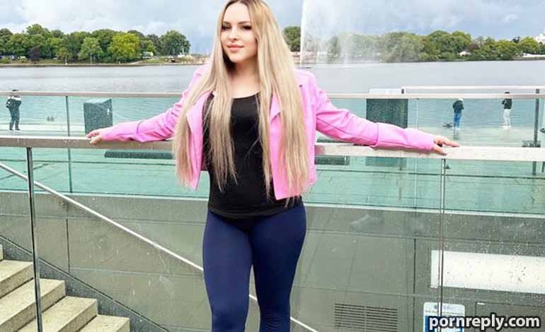 Affair Fog Vs True Love: Easy Ways To Spot The Difference Woman in a pink jacket and dark outfit stands with arms outstretched along a glass railing by a lake with a fountain in the background.