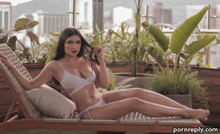 Escorts Redding: Plan The Most Amazing Date Of Your Life Right Woman in a white bikini reclining on a lounge chair on a rooftop terrace with large potted plants and a city skyline in the background.
