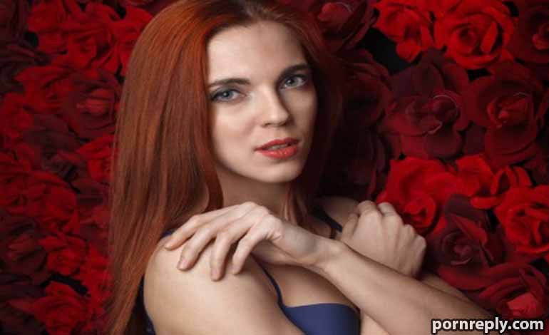 How to Market Your Shemale Sex Doll Page and Get More Fans Red-haired woman posing in front of a dense wall of red roses, arms crossed near her shoulders.